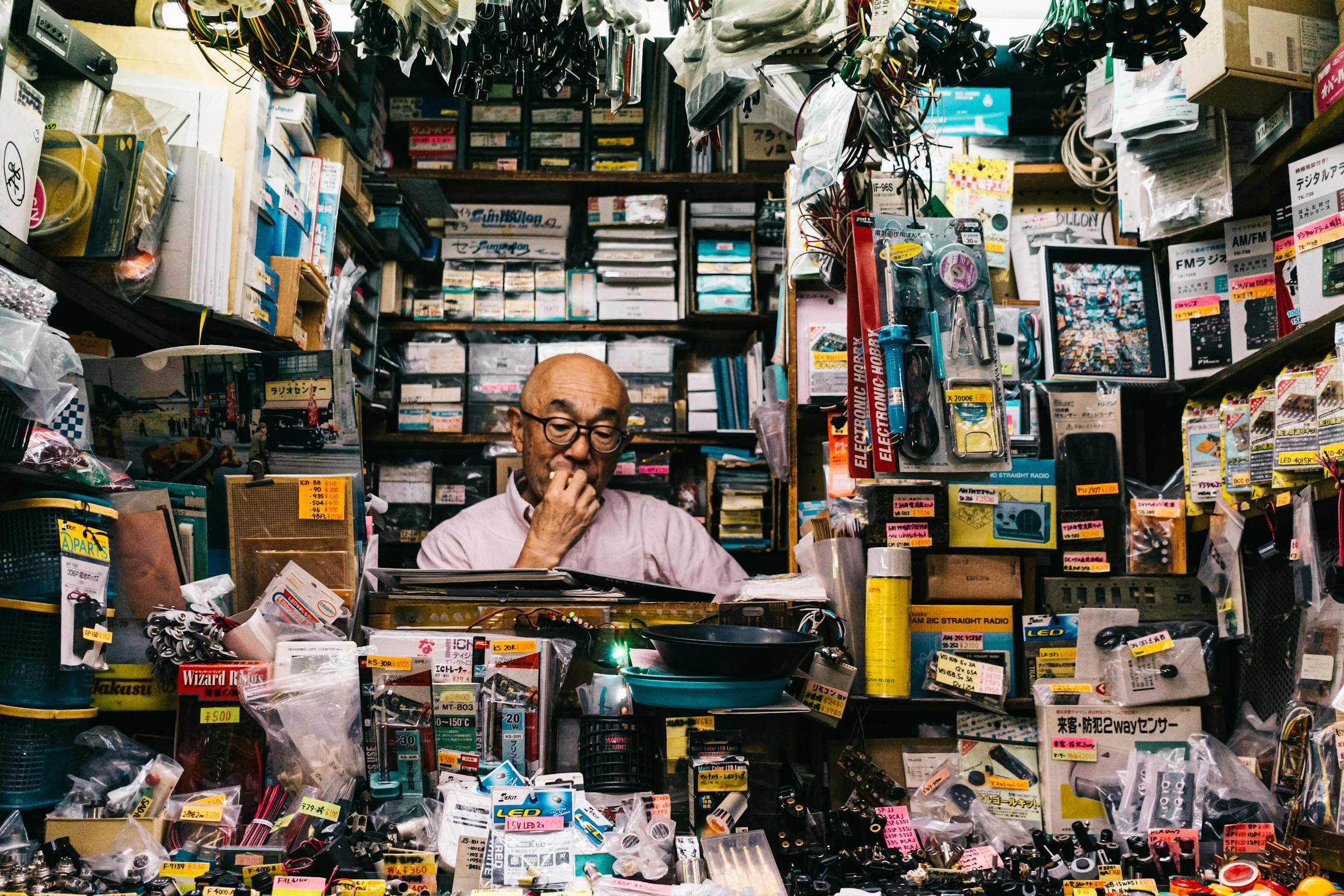 A shopkeeper behind a counter in a shop full of electronics