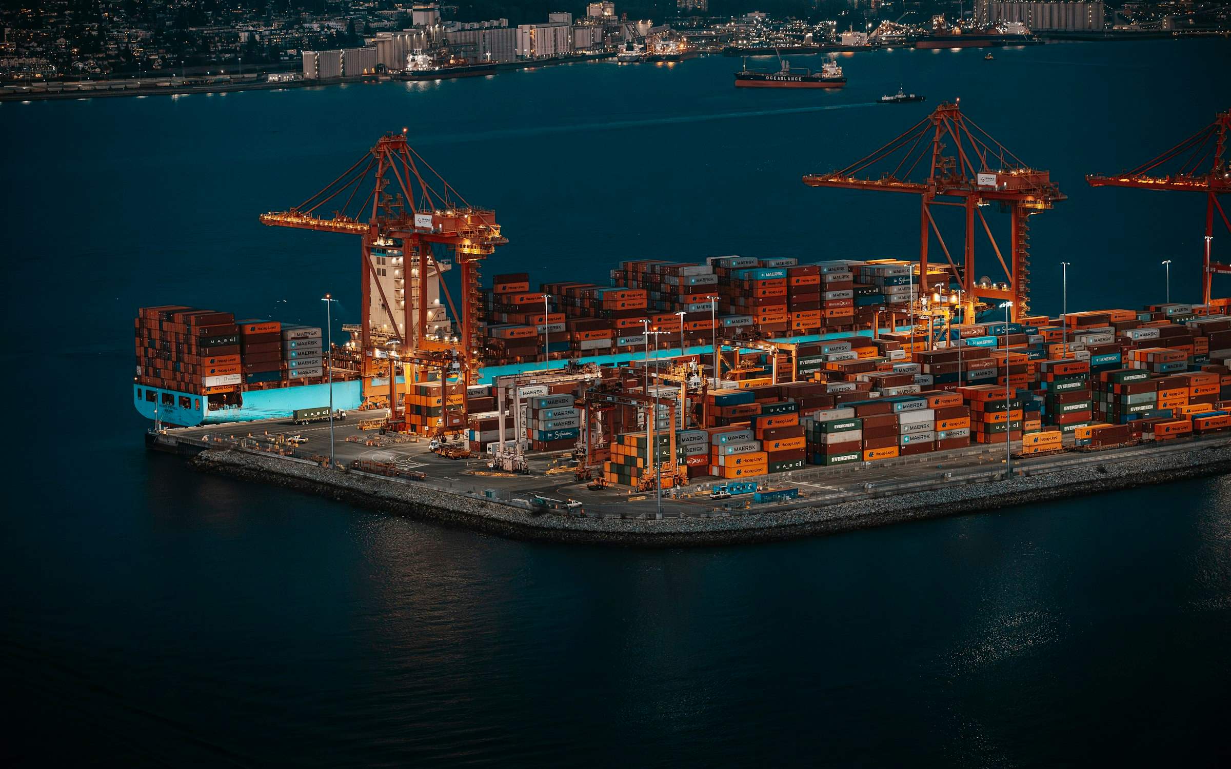 A container ship berthed under cranes at a container terminal at night